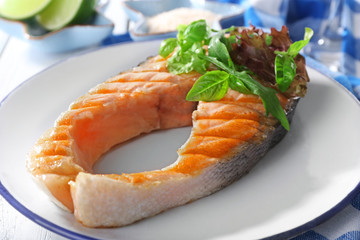 Tasty grilled salmon with greens on table close up
