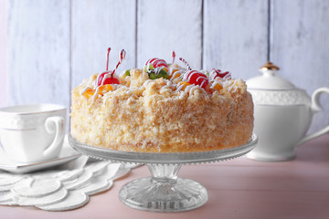 Butter cake with cherries on stand, on color wooden background