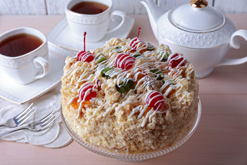 Butter cake with cherries on stand and table setting, on color wooden background
