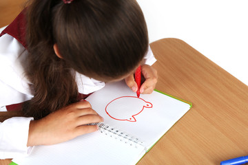 Beautiful little schoolgirl in classroom and draws in notebook