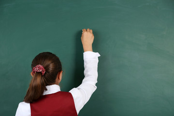 Beautiful little girl writes on blackboard in classroom