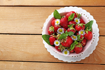 Red ripe strawberries in bowl, on color wooden background