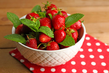 Red ripe strawberries in bowl, on color wooden background