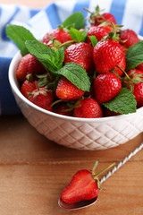 Red ripe strawberries in bowl, on color wooden background