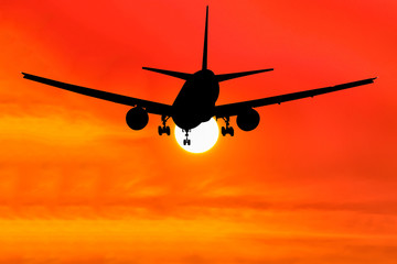 Silhouetted commercial airplane flying at sunset