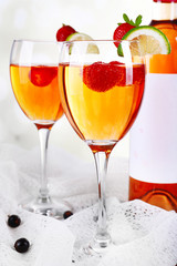 Glasses of wine with strawberries and slice of lime on light background