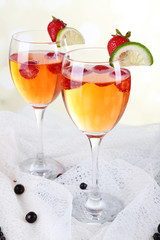 Glasses of wine with strawberries and slice of lime on light background