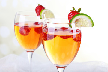 Glasses of wine with strawberries and slice of lime on light background