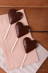 Chocolate heart shaped candies on sticks with napkin on wooden background