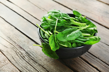 Bowl of fresh spinach leaves on wooden background