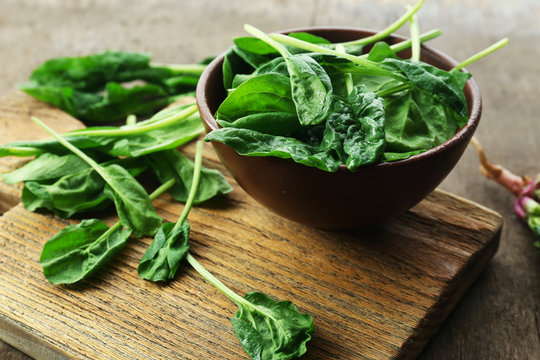 Bowl of fresh spinach leaves on wooden cutting board, closeup