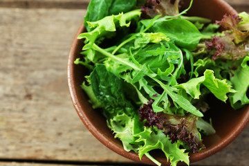 Bowl of mixed green salad on wooden table, closeup