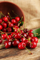Fresh cherries in bowl on wooden table with sackcloth, closeup