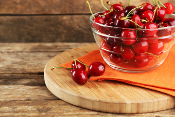 Fresh cherries in glass bowl with napkin on wooden background