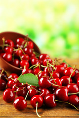 Pile of fresh cherries in bowl on wooden table on green blurred background