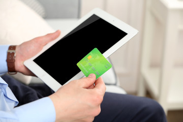 Man holding credit card and tablet on sofa in room