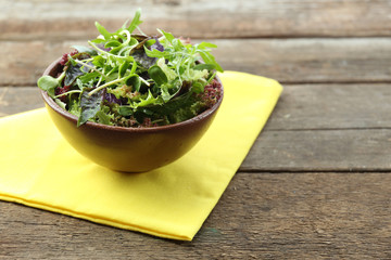 Fresh mixed green salad in bowl on wooden table close up