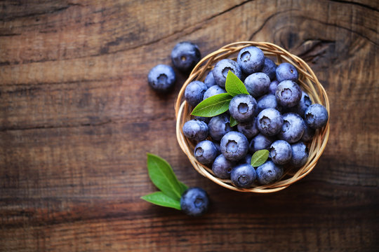 Fresh ripe garden blueberries in a wicker bowl on dark rustic wooden table. with copy space for your text
