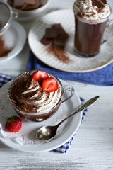 Cups of coffee with cream and fresh strawberry on color wooden background