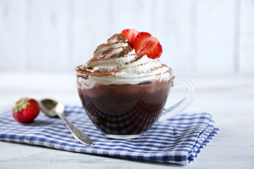 Cup of coffee with cream and fresh strawberry on color wooden background