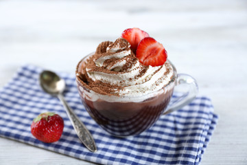 Cup of coffee with cream and fresh strawberry on color wooden background