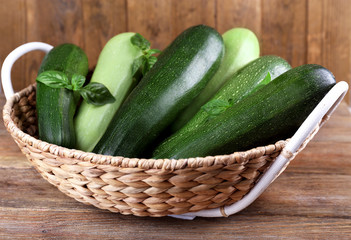 Fresh zucchini with squash and basil in wicker basket on wooden background