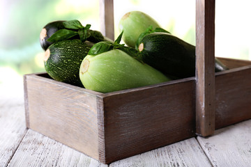 Fresh zucchini with squash and basil in wooden box on bright background
