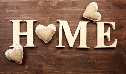 Decorative letters forming word HOME with hearts on wooden background