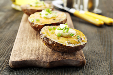 Baked potato with mayonnaise and chives on wooden cutting board, closeup