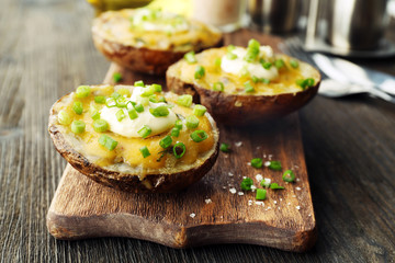 Baked potato with mayonnaise and chives on wooden cutting board, closeup