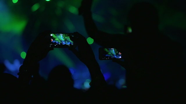 People with mobiles shooting laser show on the concert