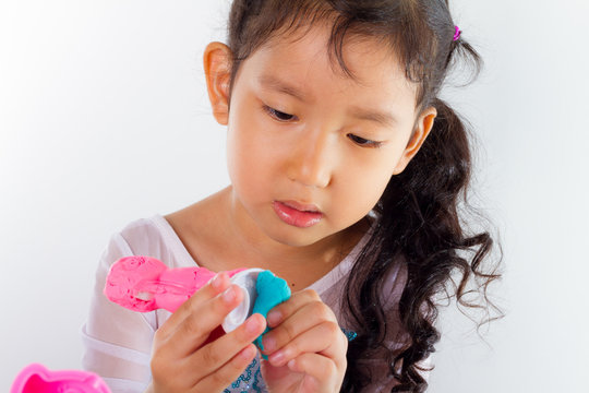 Little girl is learning to use colorful play dough on white background