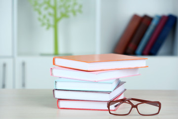 Stack of books with glasses on wooden table in room