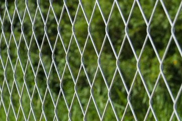 Blurred metallic mesh fence against green background