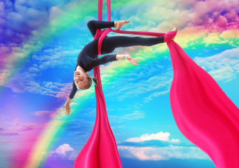 child hangs upside down on aerial silks in rainbow sky