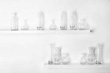 Decorative glass vases on wooden shelf  on white wallpaper background