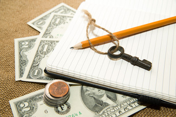Opened notebook, pencil, key and money on the old tissue