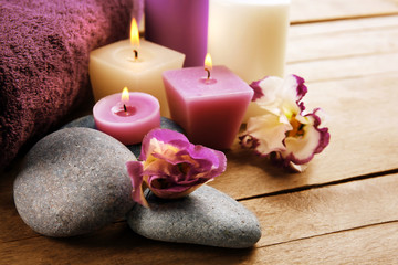 Spa still life with towels, pebbles, purple flowers and candlelight on wooden table, closeup