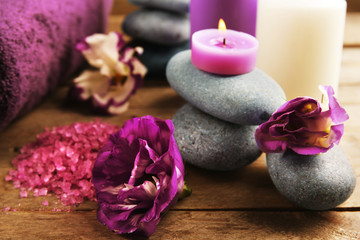 Spa still life with towels, pebbles, purple flowers and candlelight on wooden table, closeup