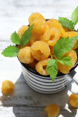 Cup of yellow raspberries on wooden table, closeup