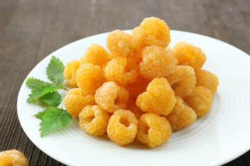 Yellow raspberries in white plate on wooden table, closeup