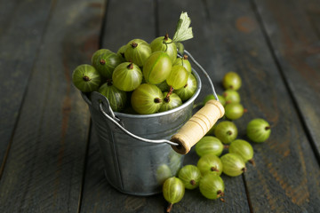 Green gooseberry in pail on wooden background