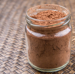 Obraz na płótnie Canvas Brown pure cocoa powder in a mason jar over wicker background