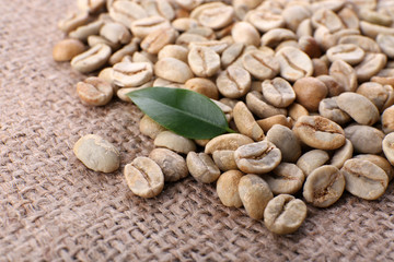 Heap of green coffee beans with leaf on sackcloth close up