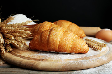 Fresh croissants with flour on wooden table on black background