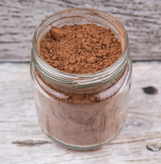 Brown pure cocoa powder in a mason jar over rustic wooden background