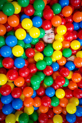 young boy having fun and hiding in hundreds of colorful plastic balls