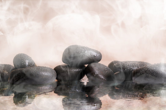 Group of black stones in warm water with steam background