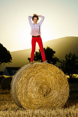Naklejka na ściany i meble Teenage girl posing at the evening on haystack, sunset colors