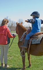 Horseback Riding Student and Teacher – A riding teacher instructs a young boy on balance when riding on his pony.